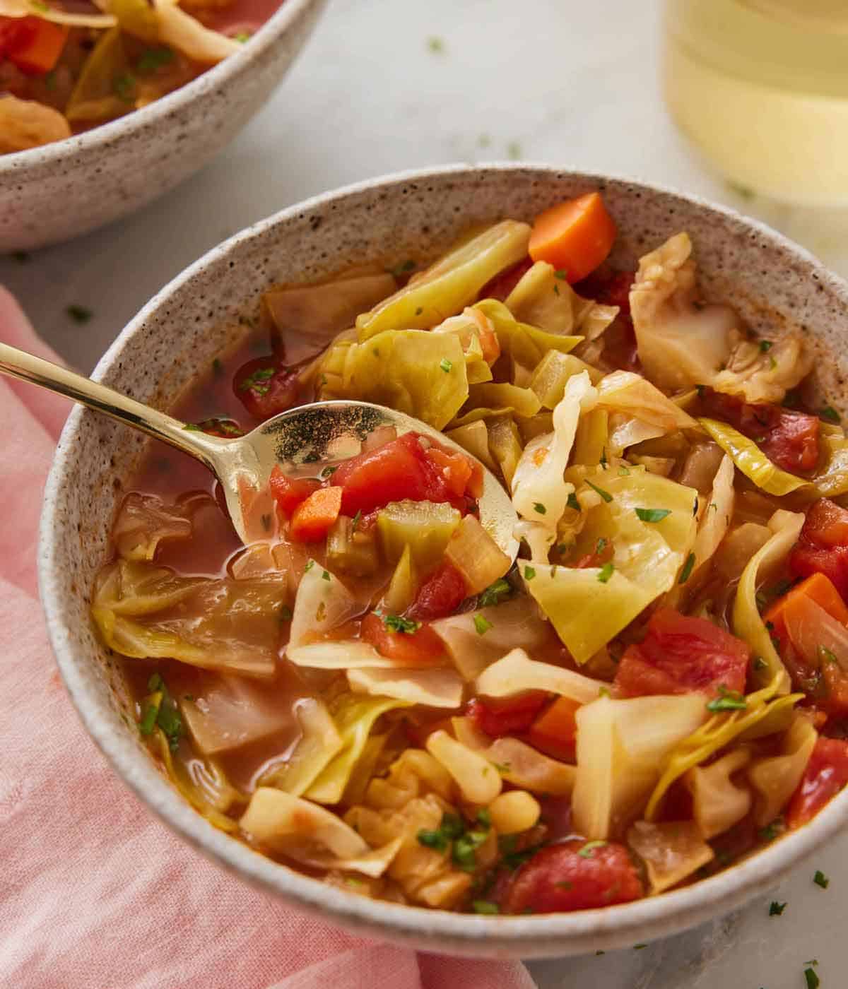 A bowl of cabbage soup with a spoon tucked under some soup.