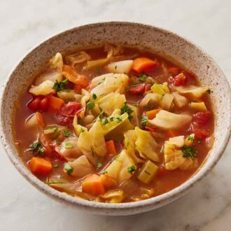 A bowl of cabbage soup with some parsley and a linen napkin off to the sides.