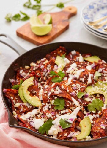A cast iron skillet with chilaquiles topped with sliced avocado and cilantro.