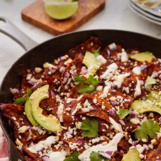 Pinterest graphic of a cast iron skillet of chilaquiles topped with creama, sliced avocado, and cilantro.