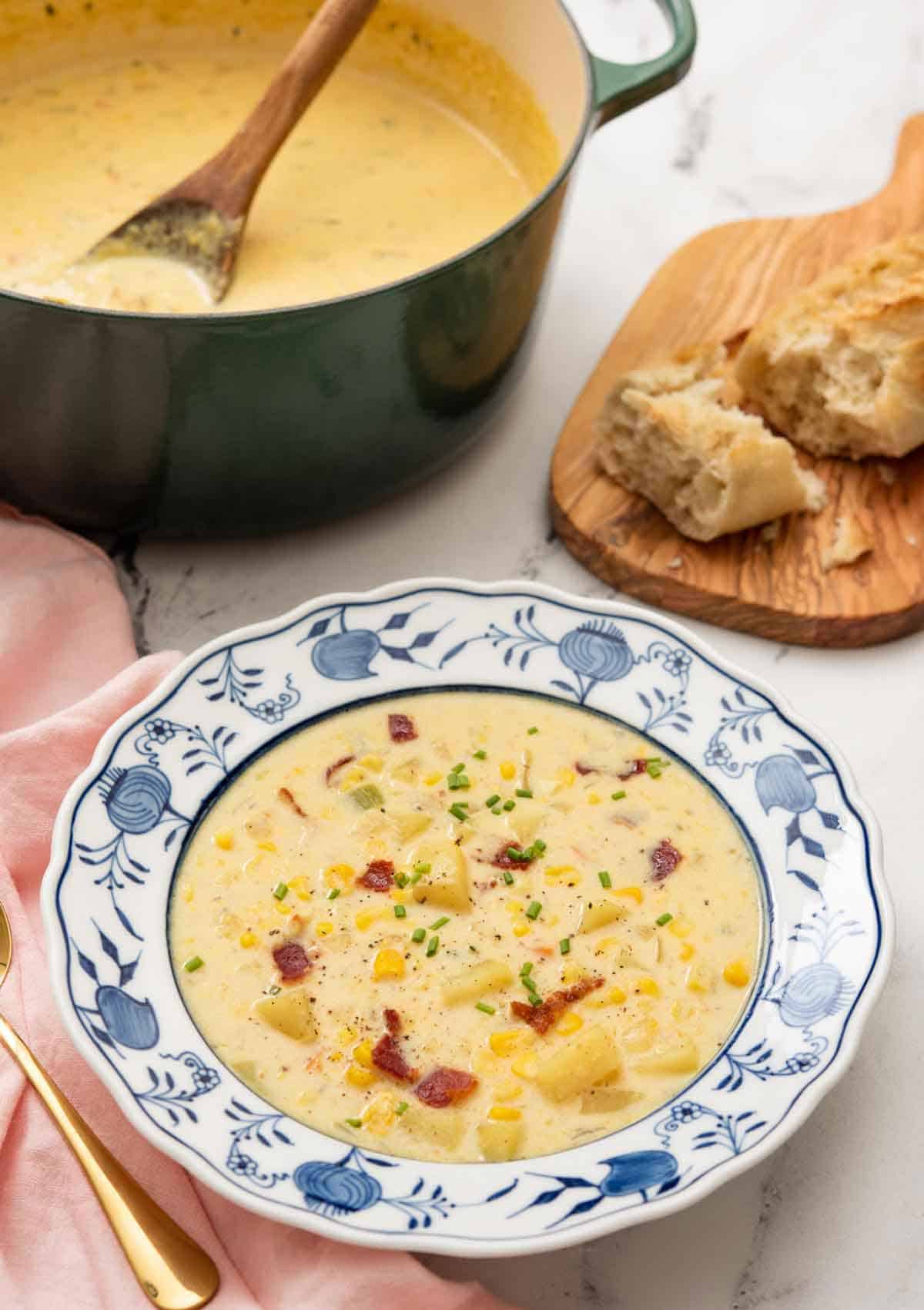A bowl of corn chowder with a green dutch oven with more chowder in the background.