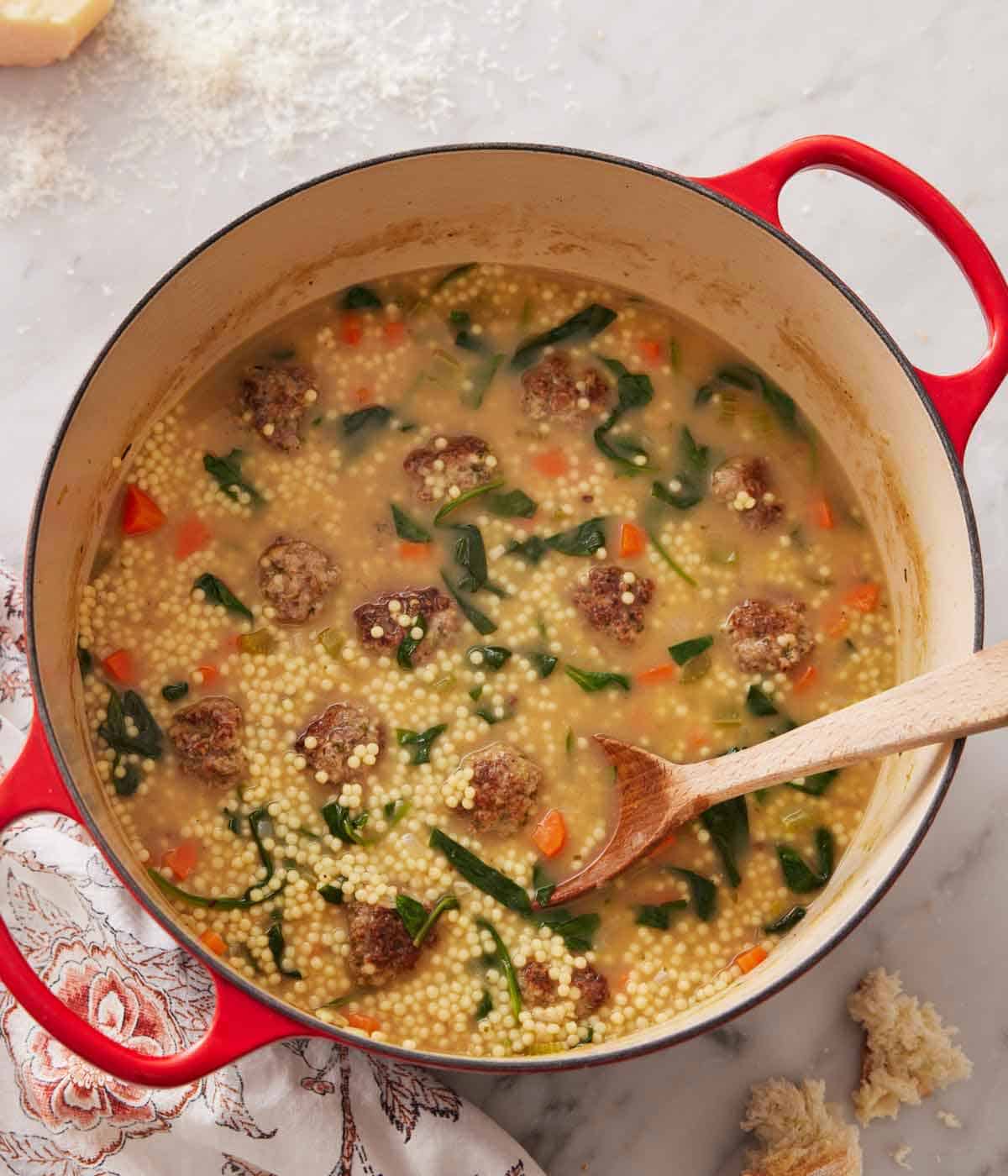 Overhead view of a pot of Italian wedding soup with a wooden spoon inside.