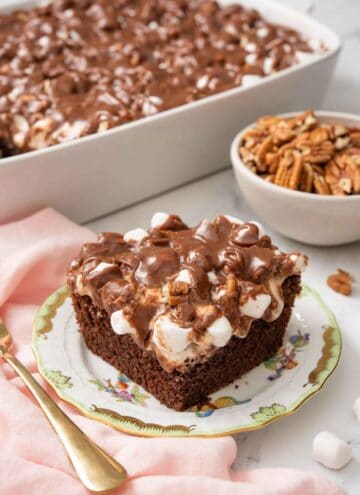 A plate with a square slice of Mississippi mud cake with the rest of the cake in the background.