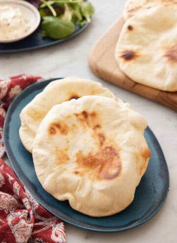 A blue platter with two pita bread on it with more in the background.