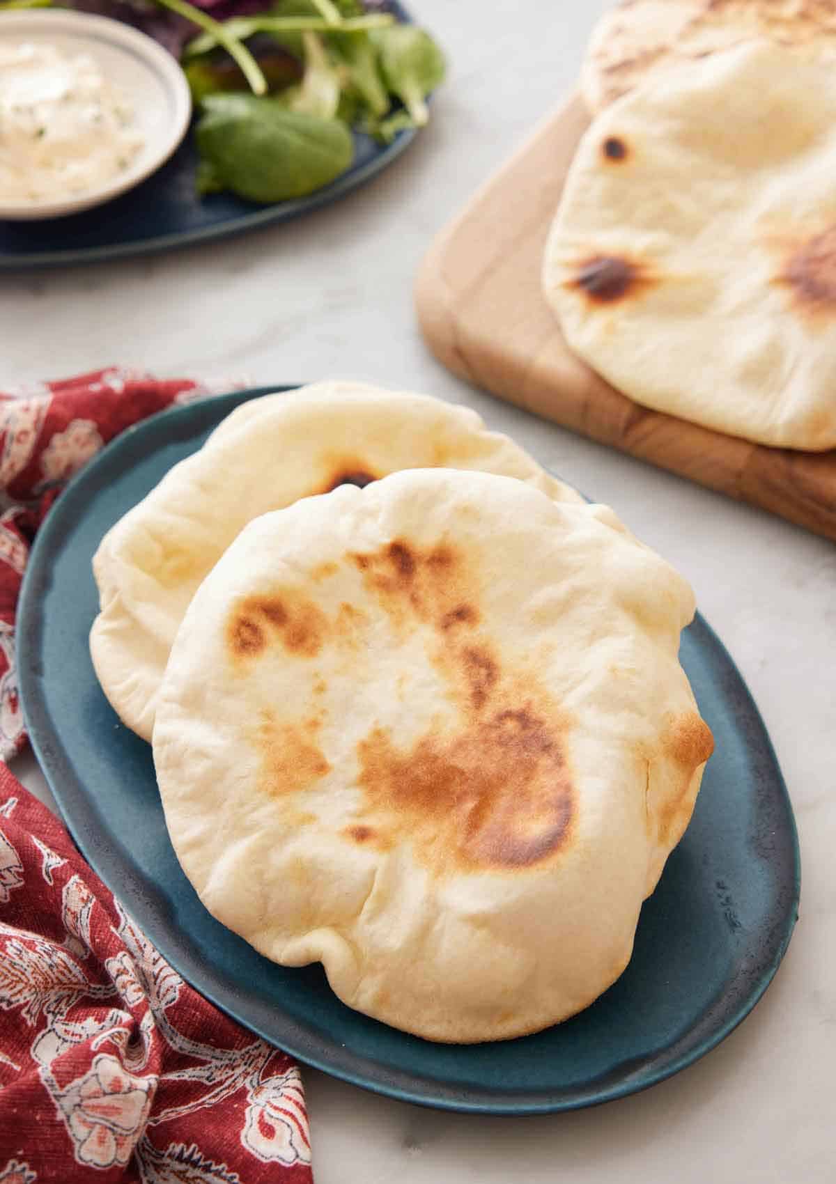 A blue platter with two pita bread on it with more in the background.