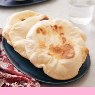 Pinterest graphic of a blue platter with three pita breads with a glass of water and some dip in the background.