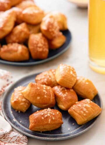 A plate of pretzel bites with a platter of more pretzel bites and a tall glass of beef in the back.