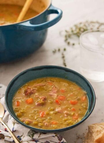 A bowl of split pea soup with a glass of water in the back along with a blue pot.