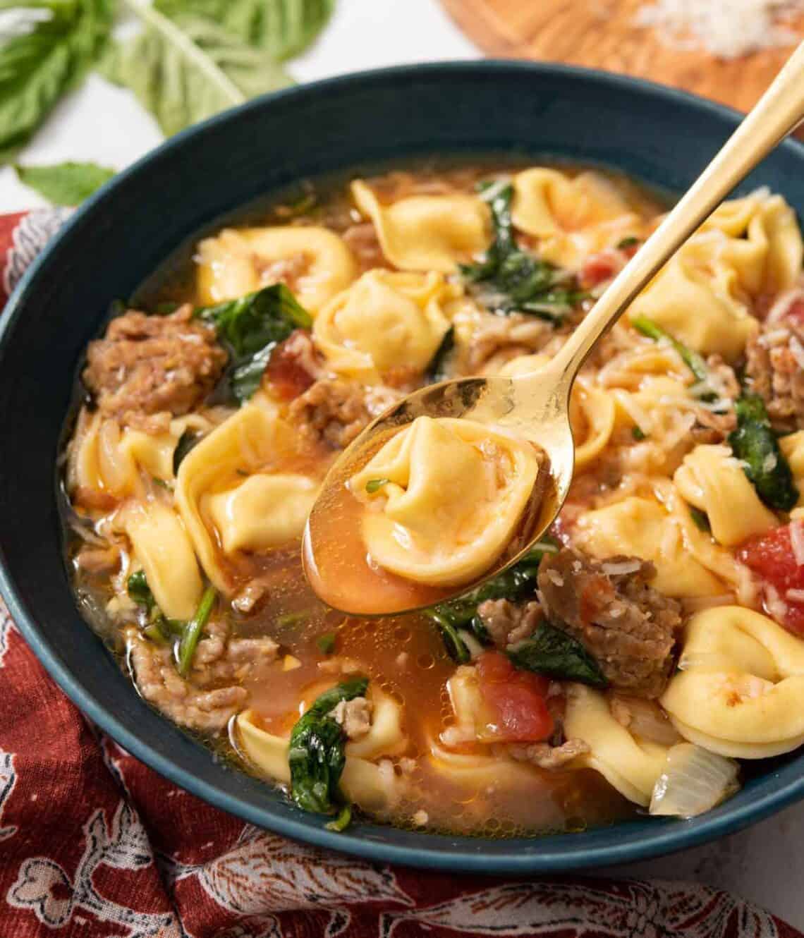 A bowl of tortellini soup with a spoonful lifted out.