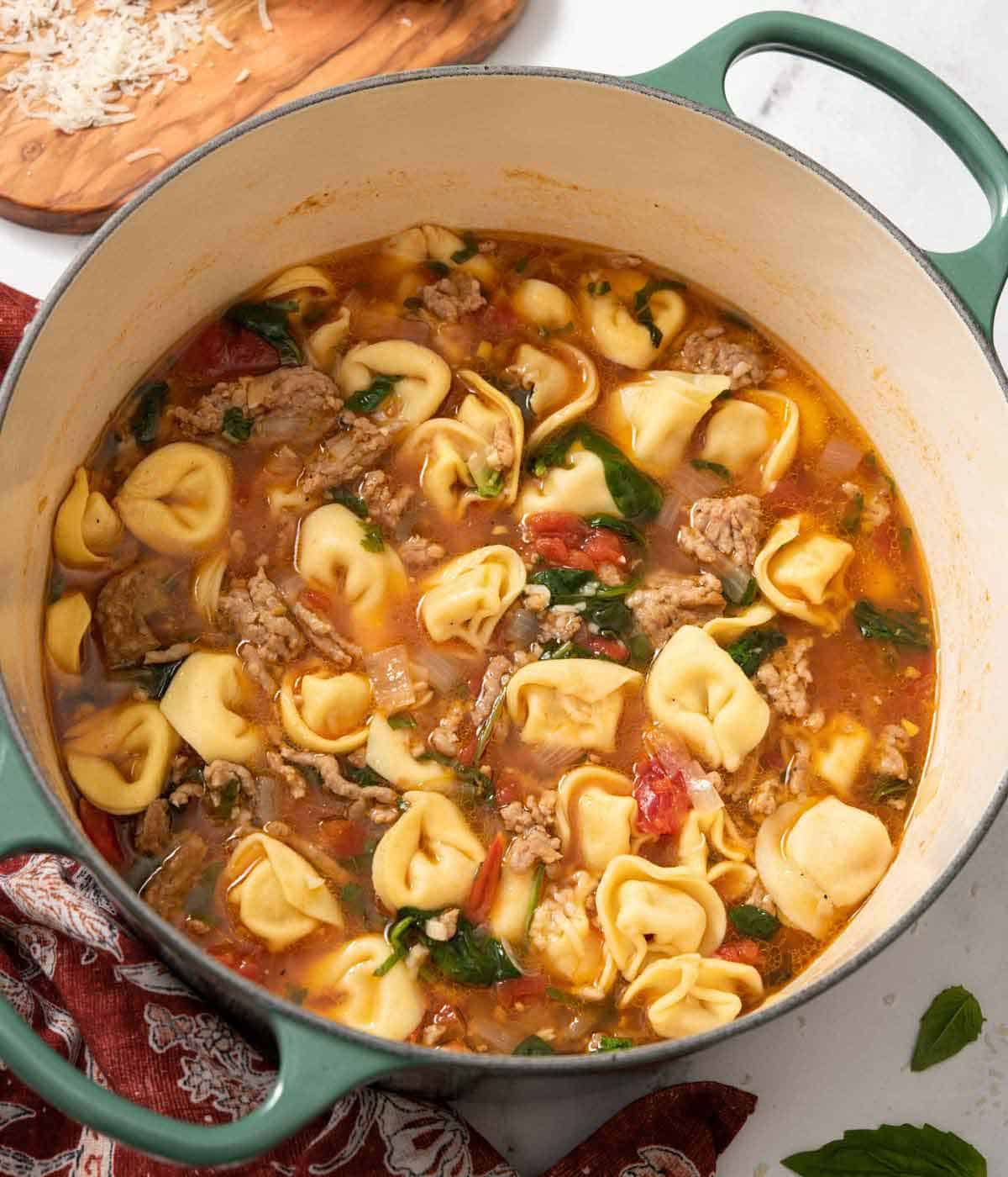 An overhead view of a green dutch oven with tortellini soup.