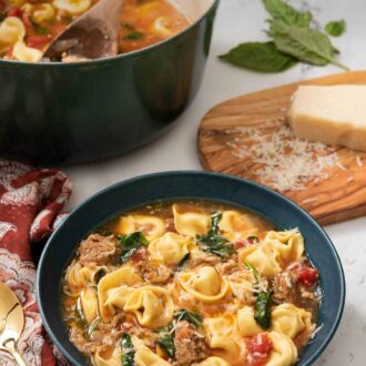 Pinterest graphic of a bowl of tortellini soup with the pot and grated parmesan in the background.