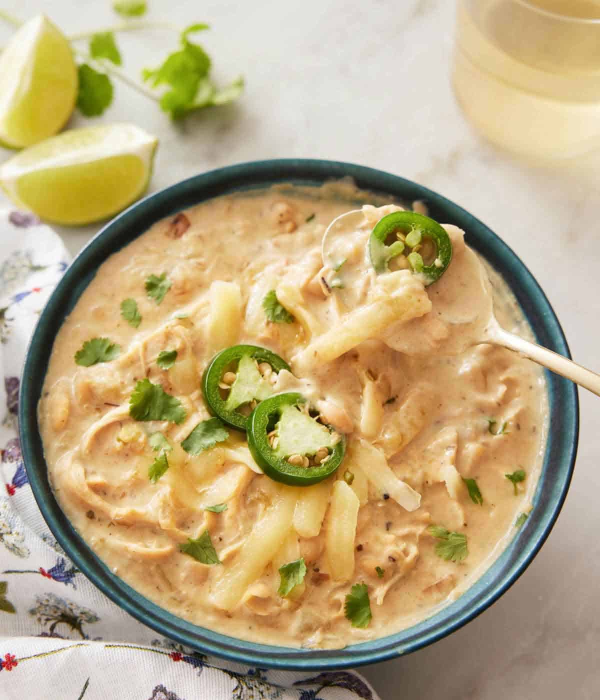 A blue bowl of white chicken chili with sliced jalapeno on top, with a spoonful being lifted up.