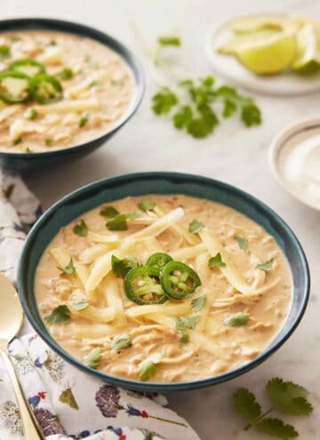 A bowl of white chicken chili with sliced jalapeno and shredded cheese on top.