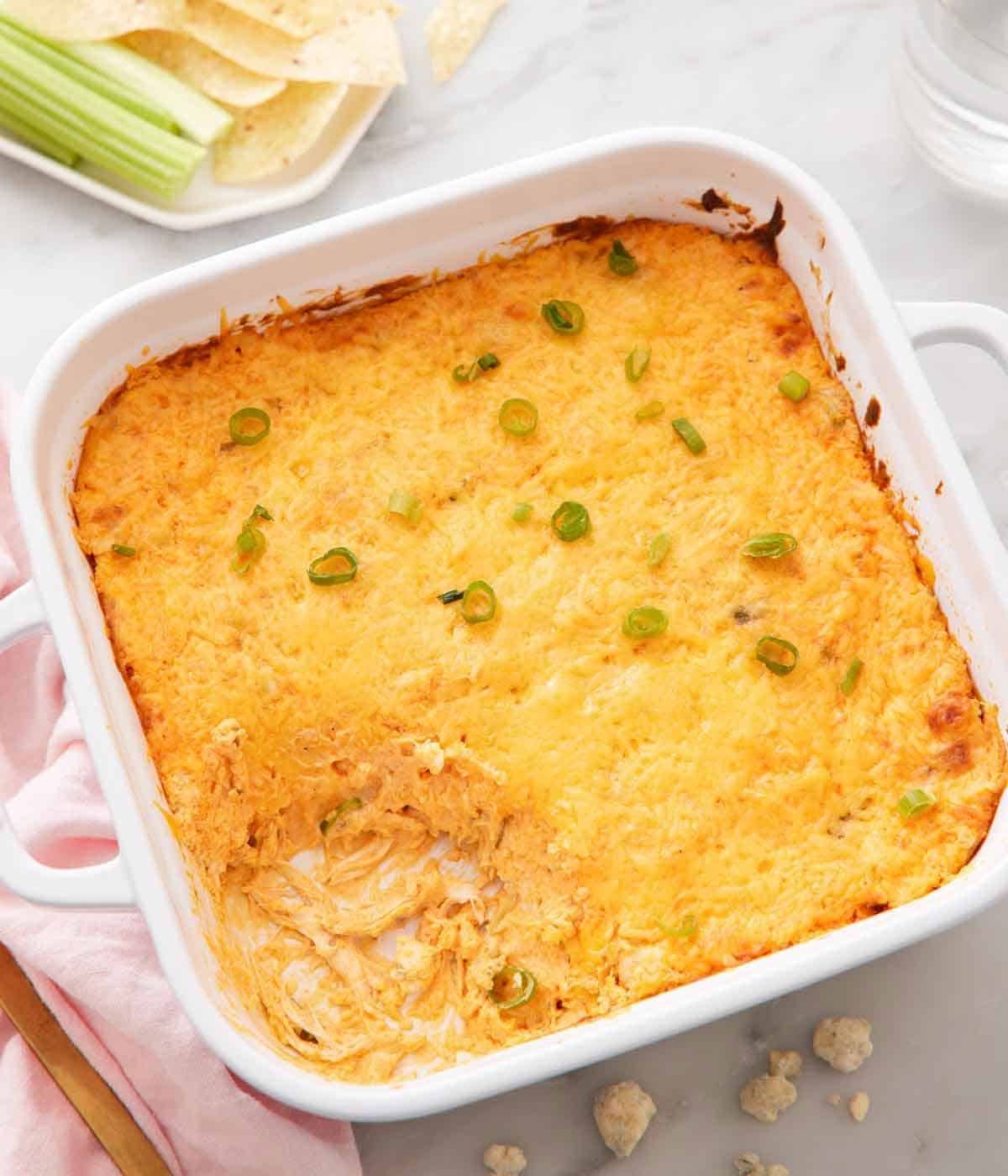 A white square baking dish full of buffalo chicken dip with a corner scooped out.