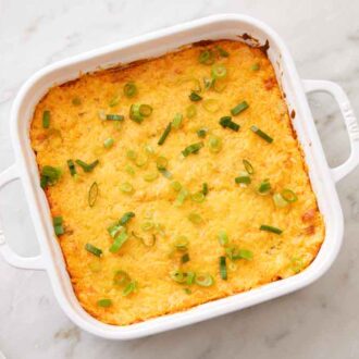 Overhead view of a white baking dish containing buffalo chicken dip topped with green onions.