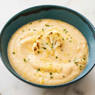 A bowl of cauliflower soup with a roasted cauliflower floret, lemon zest, and parsley garnish.