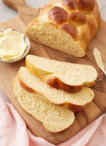 A loaf of challah on a cutting board with three slices cut in front.