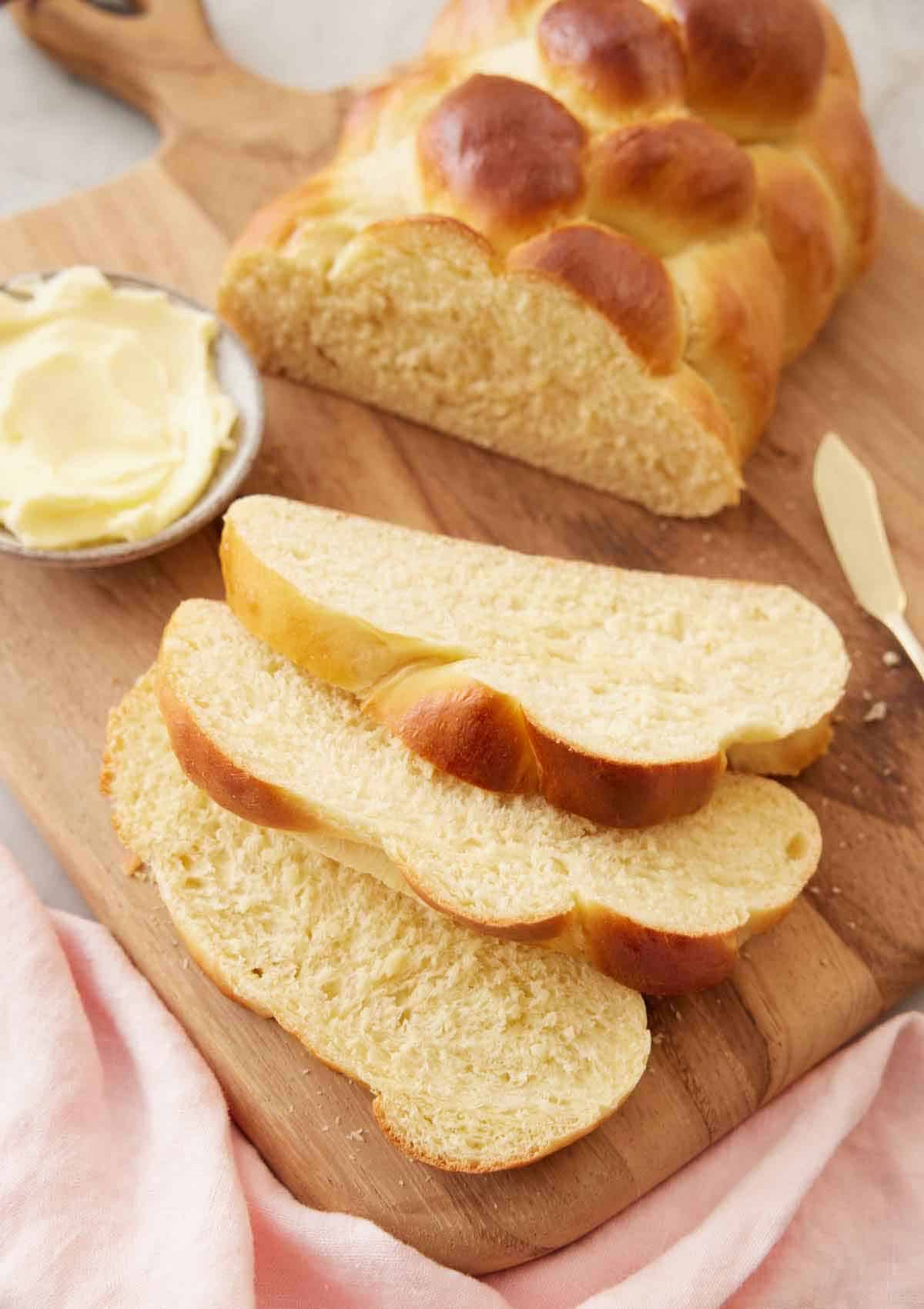 A loaf of challah on a cutting board with three slices cut in front.