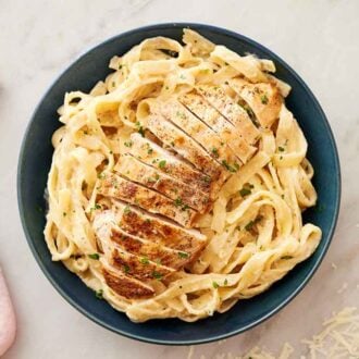 Overhead view of a bowl of chicken alfredo with a pink linen napkin and some shredded parmesan off to the side.