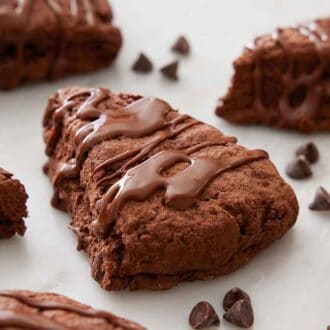 Multiple chocolate scones with chocolate drizzled on top and chocolate chips scattered around.