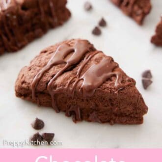 Pinterest graphic of a chocolate scone with chocolate glaze drizzled on top with more scones and chocolate chips in the background, out of focus.