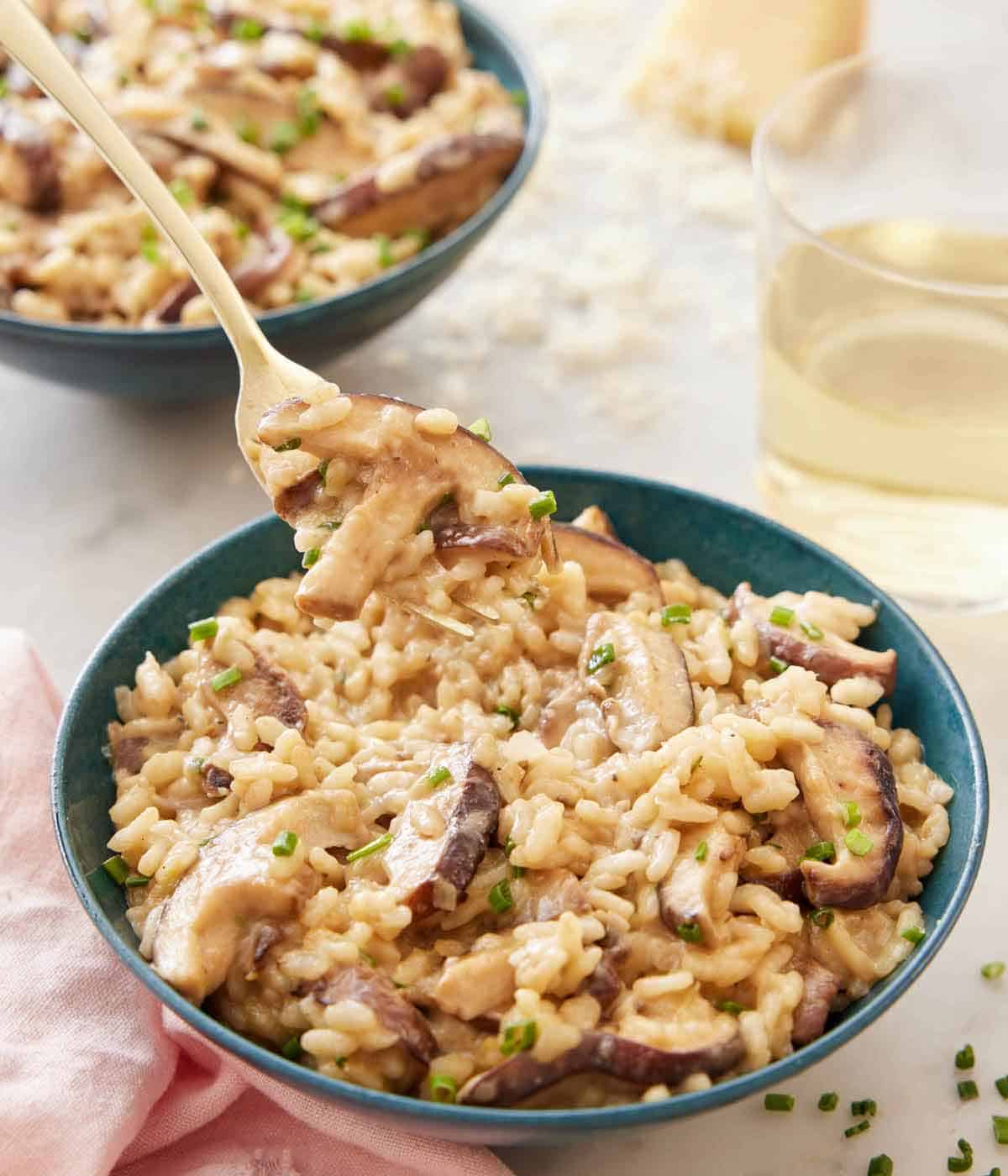 A bowl of mushroom risotto with a spoonful lifting out. A glass of wine and a second bowl in the background.