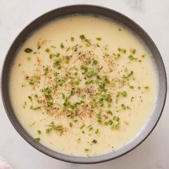 Overhead view of a bowl of potato leek soup topped with chopped chives and black pepper.