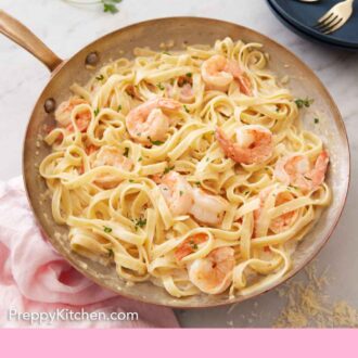 Pinterest graphic of an overhead view of a skillet of shrimp Alfredo pasta with some stacked plates and forks in the background.