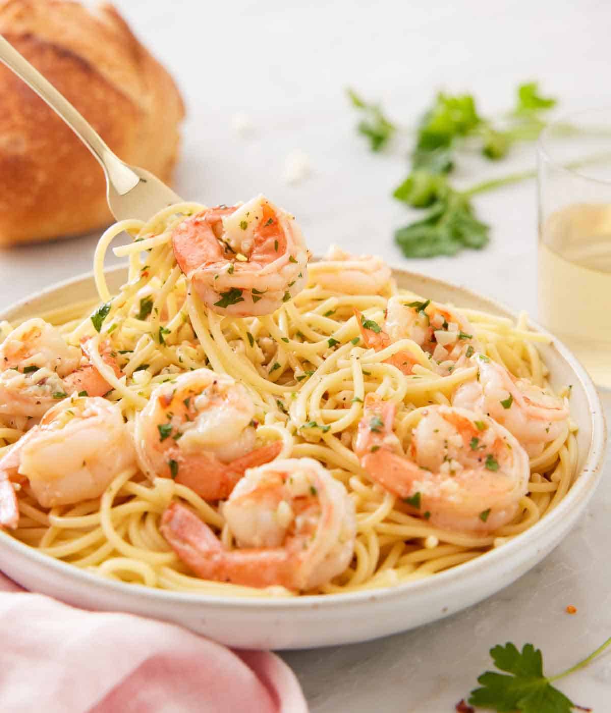 A plate with shrimp scampi and some pasta being lifted off a plate.