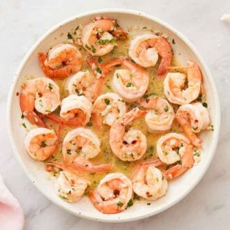 Overhead view of a plate containing shrimp scampi with torn bread and a pink linen off to the side.