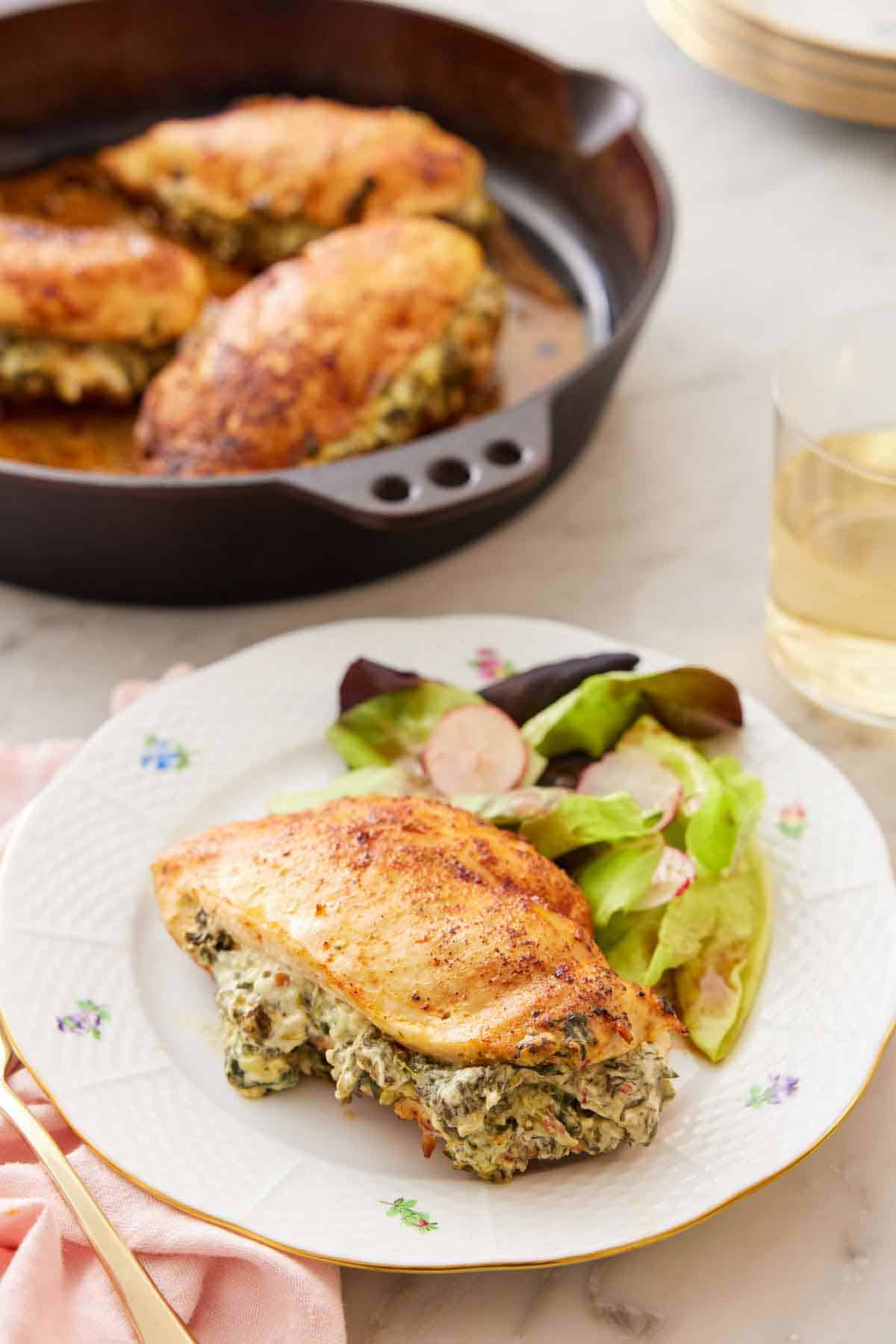 A plate with a spinach stuffed chicken breast with some salad with a cast iron with three more breasts in the background.