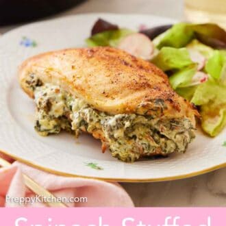 Pinterest graphic of a spinach stuffed chicken breast on a plate with the stuffing showing with some salad behind it.