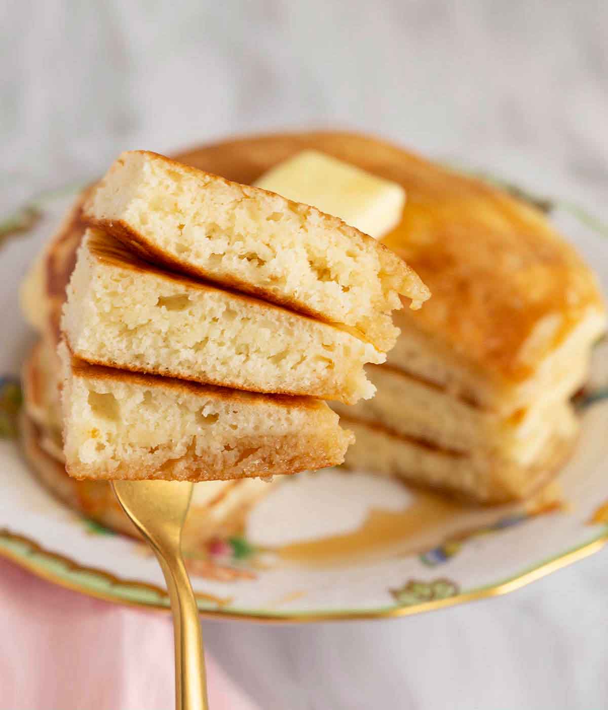 A golden fork holding three pancake pieces.