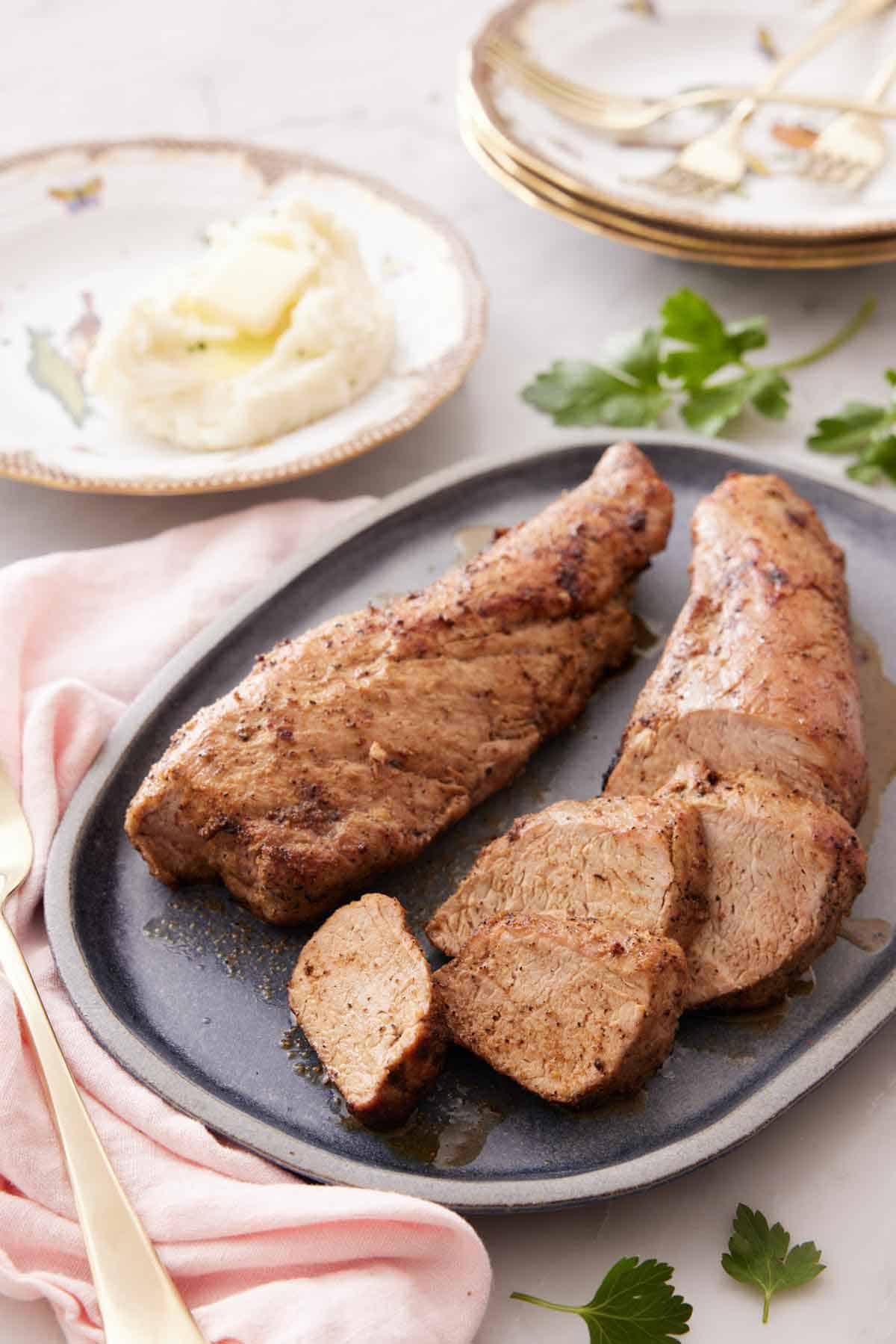 A platter with two pieces of pork tenderloin with one sliced.