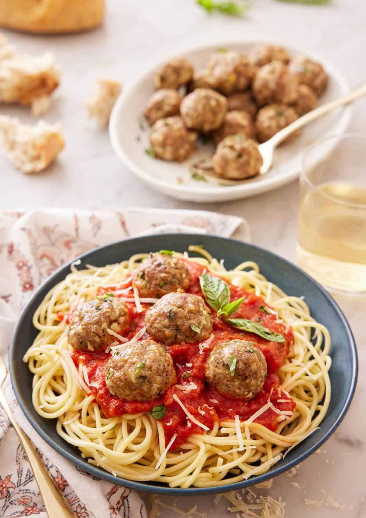A plate of noodles with tomato sauce topped with turkey meatballs and basil with a platter of meatballs in the background.