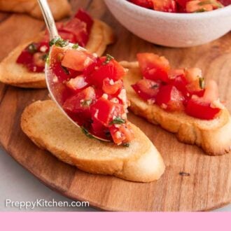 Pinterest graphic of a spoonful of bruschetta mixture added to a piece of toasted baguette.
