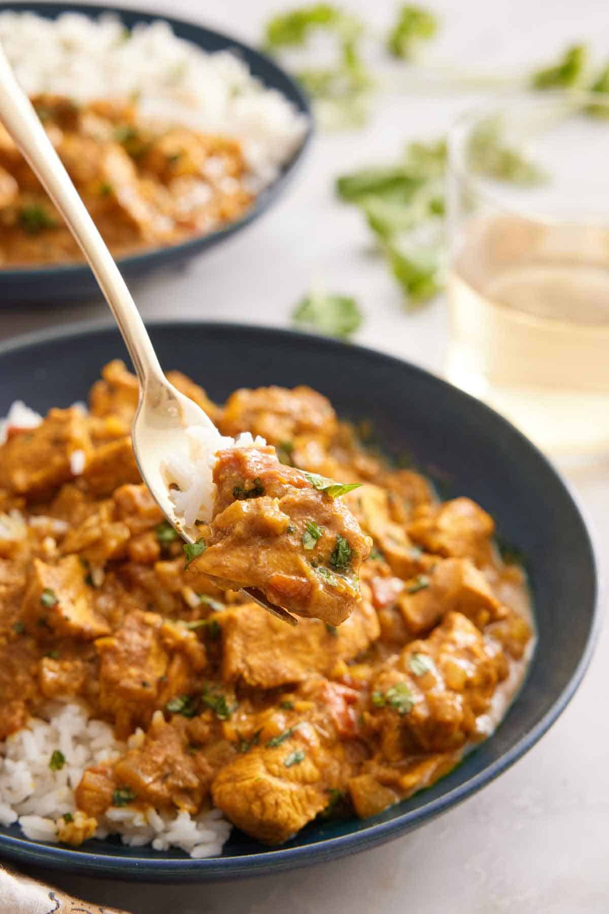 A forkful of chicken curry lifted from a bowl.