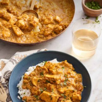 Pinterest graphic of chicken curry in a bowl over rice with a glass of wine and skillet with more curry in the background.