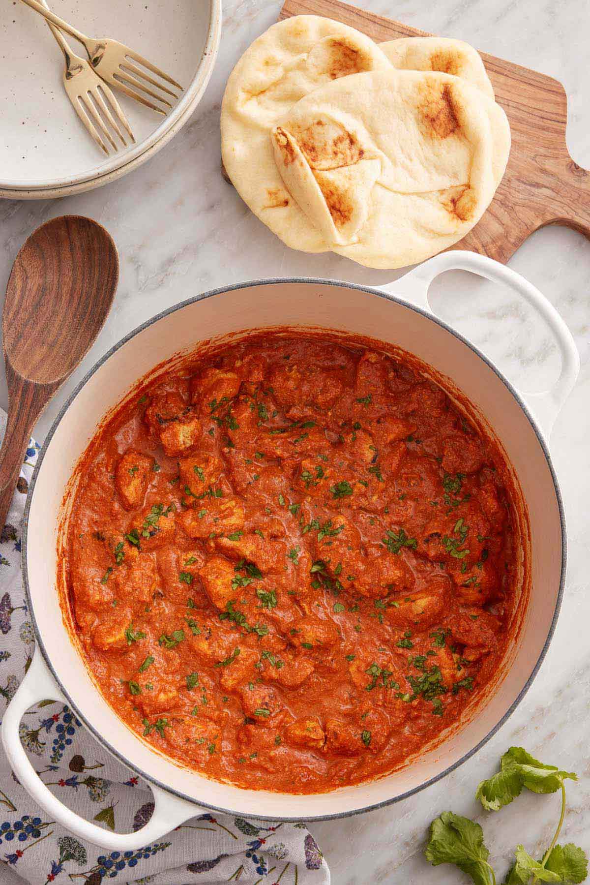Overhead view of chicken tikka masala in a white Dutch oven garnished with cilantro with naan beside it.