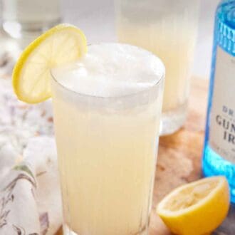 Pinterest graphic of a glass of Gin Fizz with a bottle of gin, cut lemons, and another cocktail in the background.