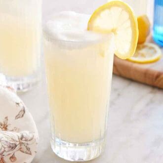 A glass of Gin Fizz with a lemon slice garnish and a second glass and a bottle of gin in the back.