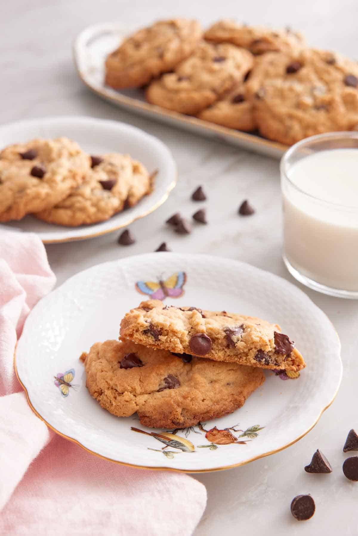 A plate with a peanut butter chocolate chip cookie cut in half, stacked so it shows the middle cut-side. More cookies in the background.