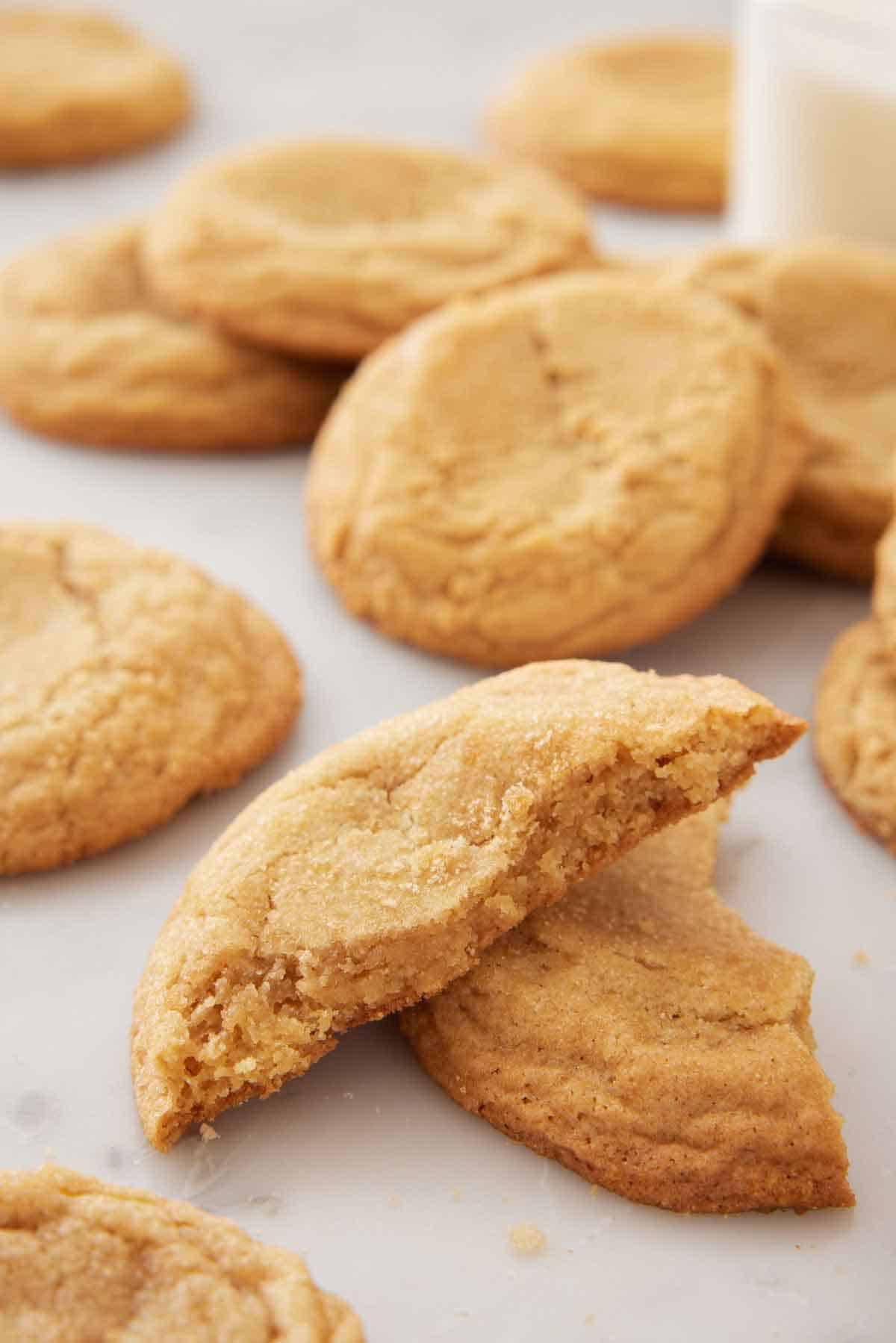 A brown sugar cookie broken in half, with one half stacked on top of the other. More cookies in the back.