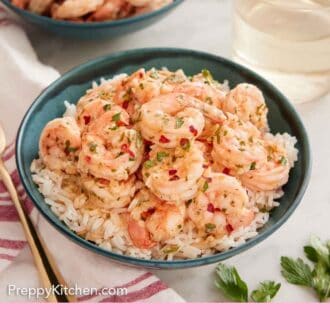 Pinterest graphic of a bowl of rice with garlic shrimp on top with more shrimp and wine in the background.