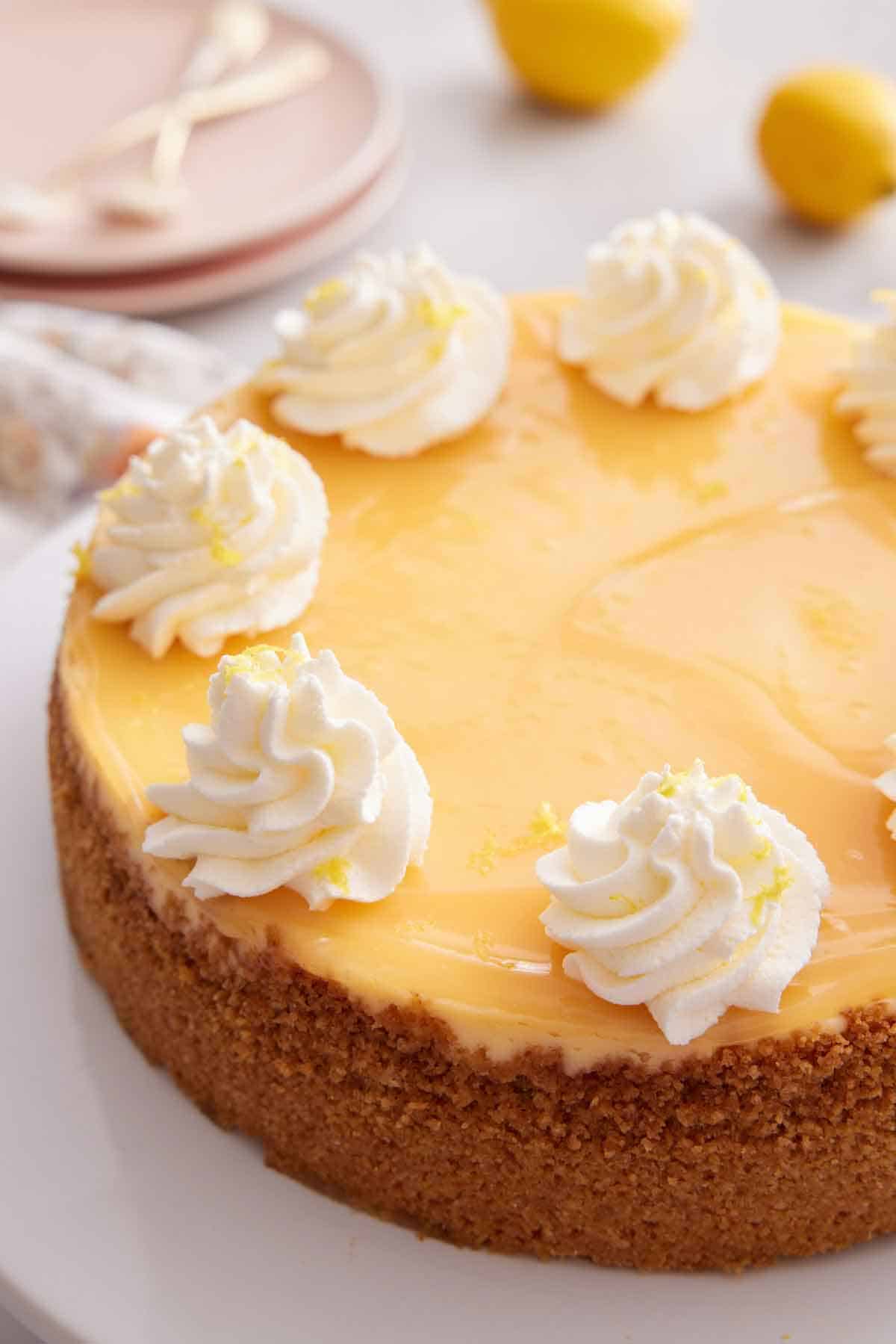A lemon cheesecake with dollops of whipped cream and lemon zest on the edge of the cake.