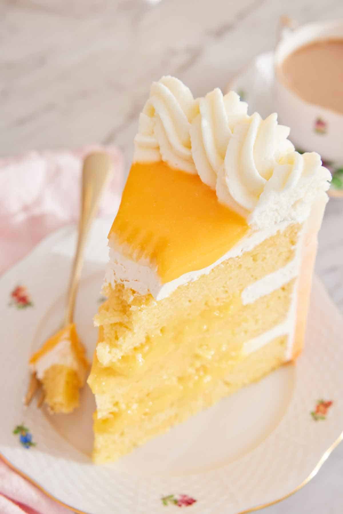 A slice of orange creamsicle cake on a plate with a forkful taken off the tip, with the fork placed beside the cake.