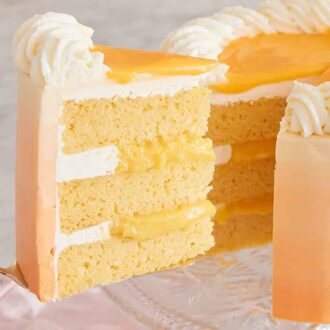 A slice of orange creamsicle cake pulled from the rest of the cake on a cake stand.