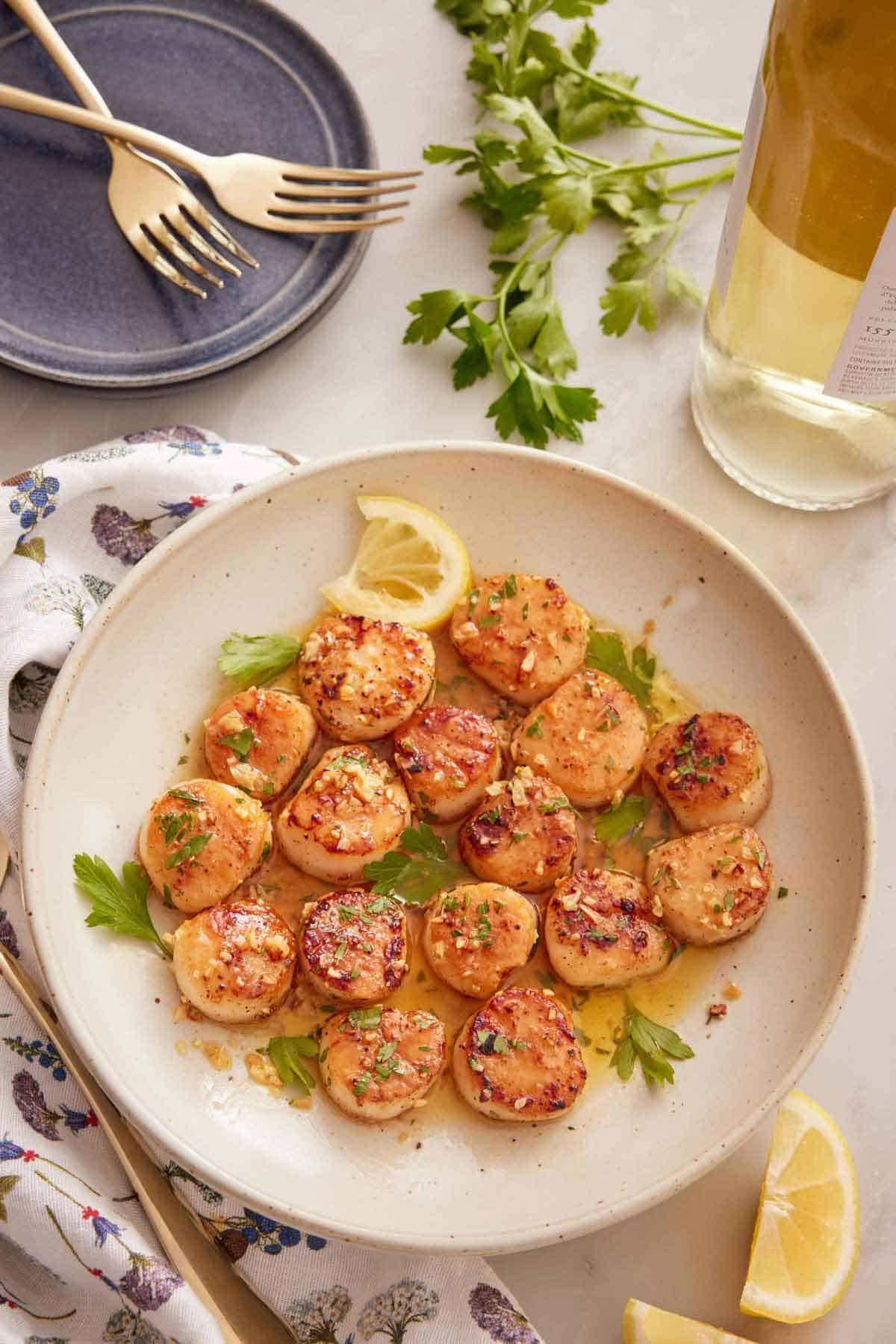 Overhead view of a plate of seared scallops with parsley and sliced lemon on top.