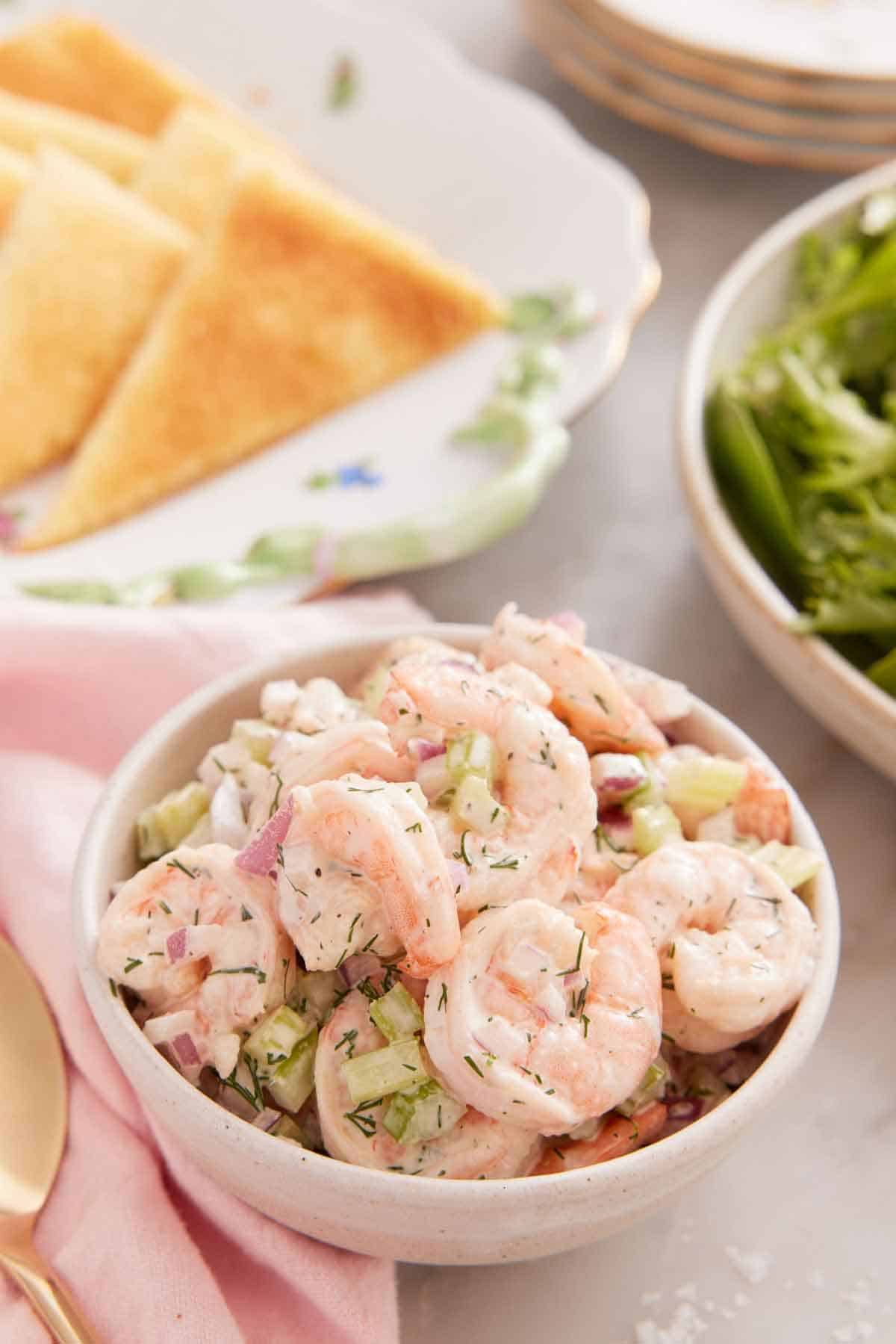 A bowl of shrimp salad with a plate of bread in the back.