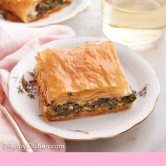 Pinterest graphic of a plate of spanakopita with a glass of wine and another plate in the background.